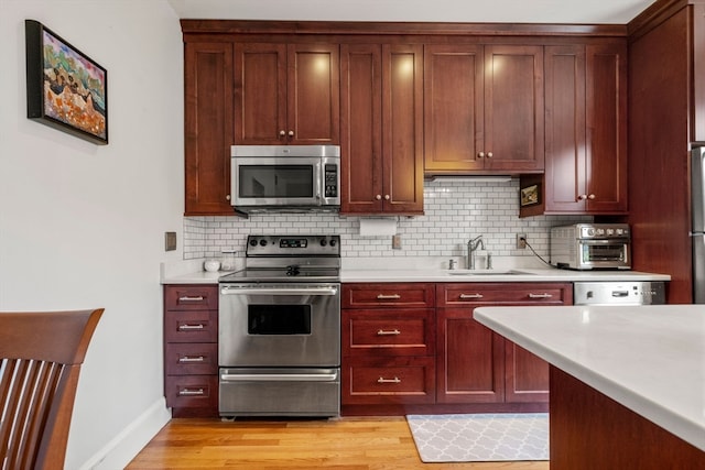 kitchen featuring appliances with stainless steel finishes, backsplash, light wood-type flooring, and sink