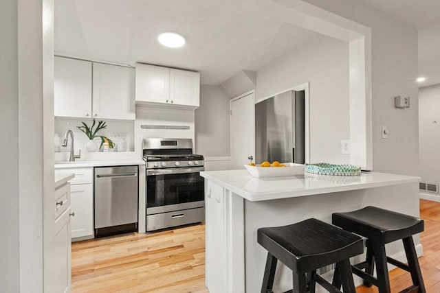 kitchen featuring white cabinets, a kitchen breakfast bar, stainless steel appliances, and light hardwood / wood-style floors