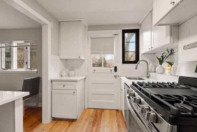 kitchen with sink, light hardwood / wood-style flooring, decorative backsplash, white cabinetry, and stainless steel range with gas stovetop