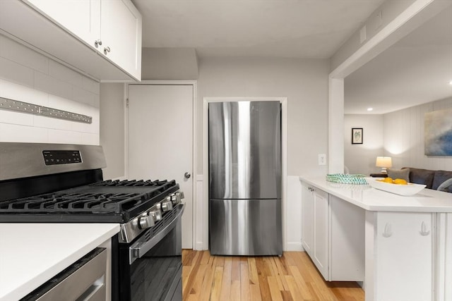 kitchen featuring white cabinets, light wood-type flooring, tasteful backsplash, kitchen peninsula, and stainless steel appliances