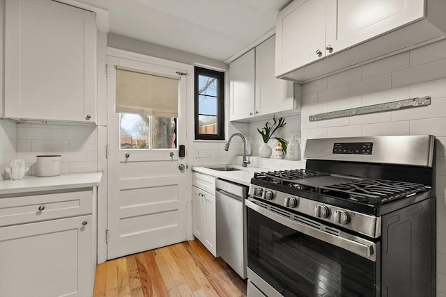 kitchen with light wood-type flooring, tasteful backsplash, stainless steel appliances, sink, and white cabinetry