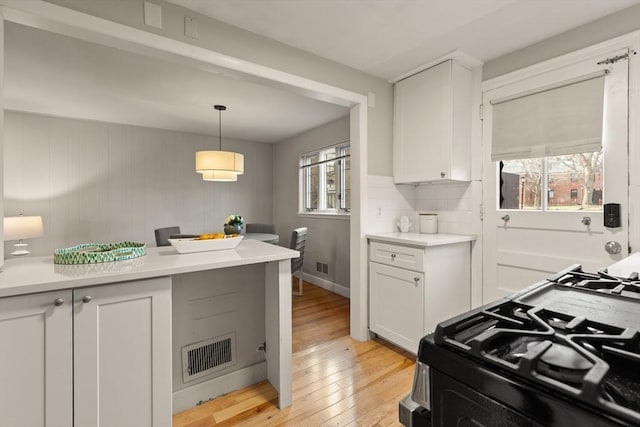 kitchen with pendant lighting, light wood-type flooring, tasteful backsplash, gas stove, and white cabinetry