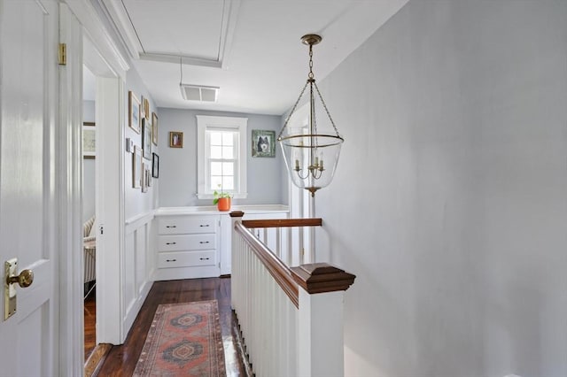 corridor featuring dark wood finished floors, an upstairs landing, attic access, and a chandelier