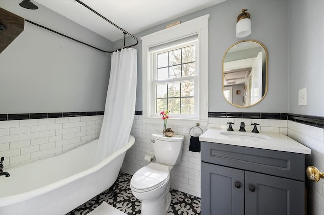 full bath featuring a tub, tile walls, wainscoting, toilet, and vanity