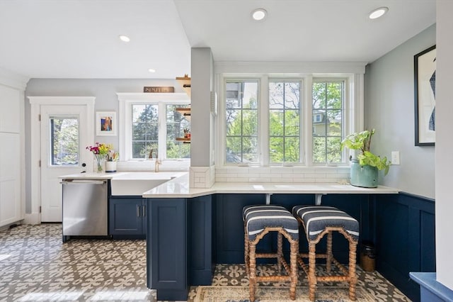 kitchen with stainless steel dishwasher, a sink, light countertops, decorative backsplash, and recessed lighting