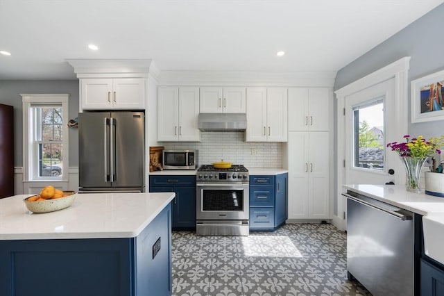 kitchen with premium appliances, blue cabinetry, under cabinet range hood, light floors, and white cabinets