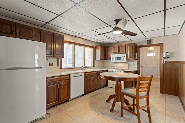 kitchen featuring white appliances, ceiling fan, light countertops, a paneled ceiling, and wainscoting