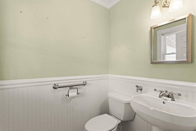 bathroom with wainscoting, toilet, ornamental molding, and a sink