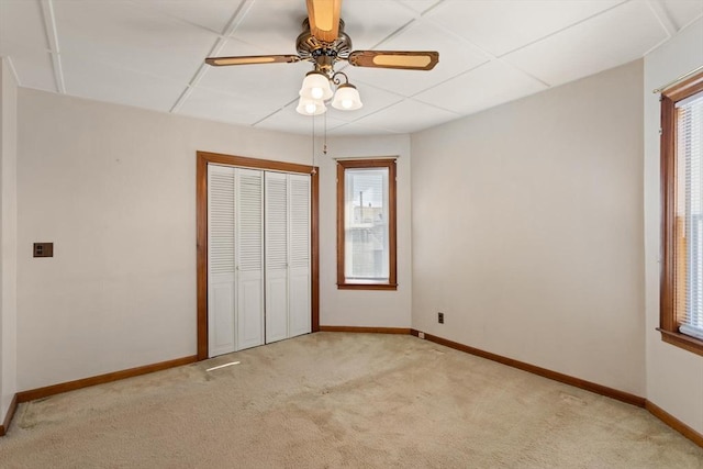 unfurnished bedroom featuring a closet, baseboards, a paneled ceiling, light colored carpet, and ceiling fan