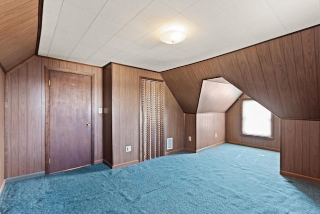 additional living space with visible vents, lofted ceiling, carpet floors, wooden walls, and baseboards