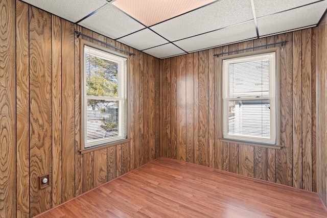 spare room featuring a drop ceiling, wood finished floors, and wood walls