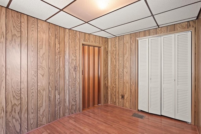 unfurnished bedroom with visible vents, wood walls, wood finished floors, and a drop ceiling