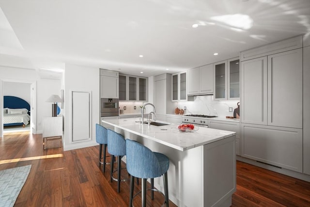 kitchen featuring dark wood-type flooring, gray cabinets, a kitchen bar, stainless steel oven, and a sink