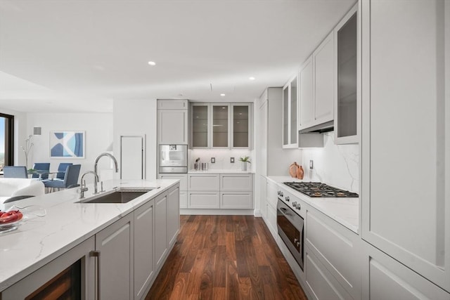 kitchen featuring glass insert cabinets, dark wood-style flooring, light stone countertops, gas cooktop, and a sink