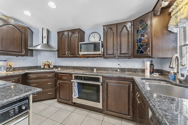 kitchen featuring sink, light tile patterned floors, stainless steel appliances, dark brown cabinetry, and wall chimney exhaust hood