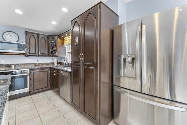 kitchen with sink, light tile patterned floors, stainless steel appliances, dark brown cabinetry, and dark stone counters