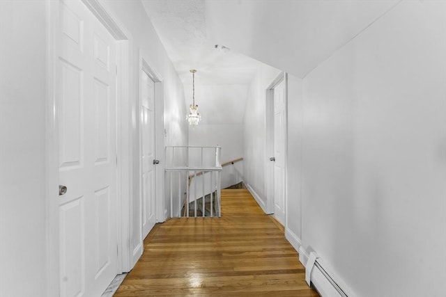 hallway with vaulted ceiling, a chandelier, wood-type flooring, and baseboard heating