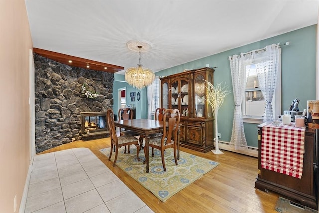 dining space featuring a baseboard radiator, a stone fireplace, an inviting chandelier, and light hardwood / wood-style floors