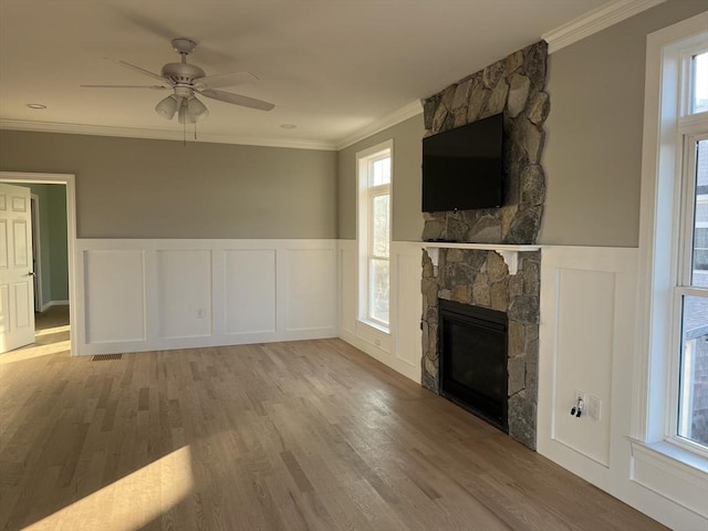 unfurnished living room with crown molding, a fireplace, ceiling fan, and light wood-type flooring