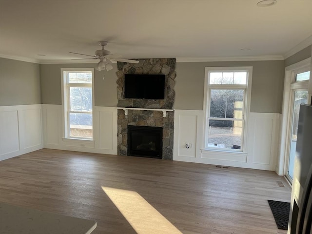 unfurnished living room featuring ceiling fan, a stone fireplace, and crown molding