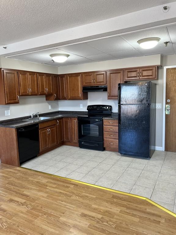 kitchen with dark countertops, under cabinet range hood, light wood-type flooring, black appliances, and a sink