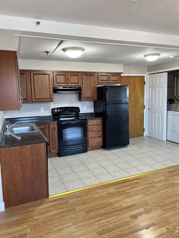 kitchen featuring washer / clothes dryer, a sink, black appliances, dark countertops, and exhaust hood