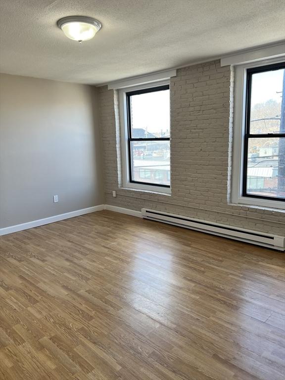 unfurnished room with a wealth of natural light, a baseboard heating unit, a textured ceiling, and wood finished floors