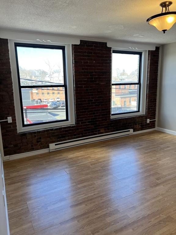 empty room with brick wall, baseboards, wood finished floors, a textured ceiling, and a baseboard radiator