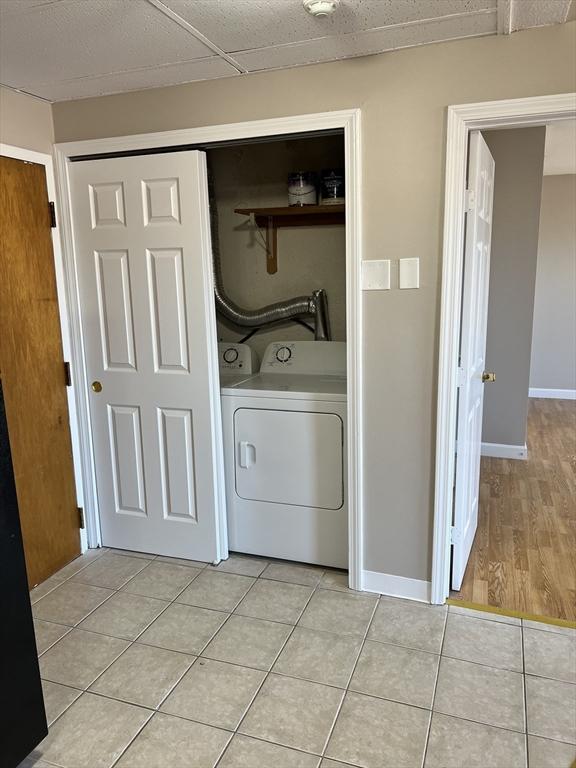 clothes washing area with light tile patterned floors, baseboards, washer / clothes dryer, and laundry area