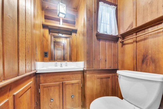 half bathroom featuring wood walls, vanity, and toilet