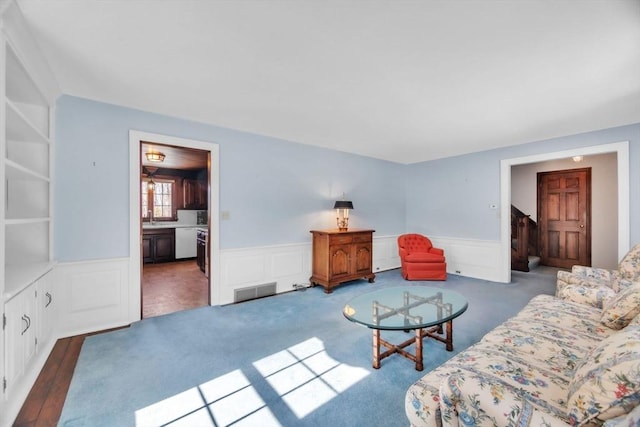 living area with a wainscoted wall, visible vents, and wood finished floors