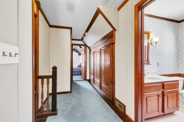 hallway featuring light carpet, a sink, visible vents, ornamental molding, and wallpapered walls