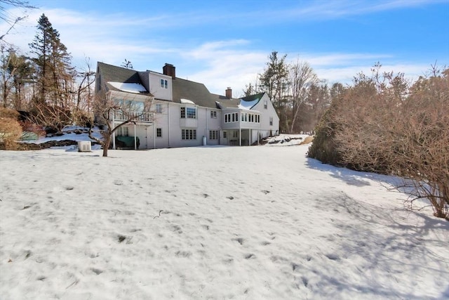 snow covered back of property with a balcony and a chimney