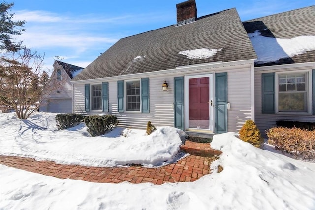 new england style home featuring a garage, roof with shingles, and a chimney