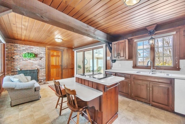 kitchen with a kitchen island, stainless steel stovetop, light countertops, a brick fireplace, and a sink