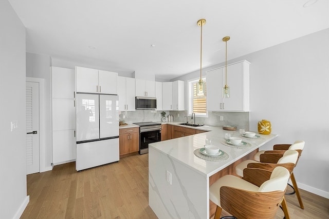 kitchen featuring appliances with stainless steel finishes, light hardwood / wood-style floors, white cabinetry, and hanging light fixtures