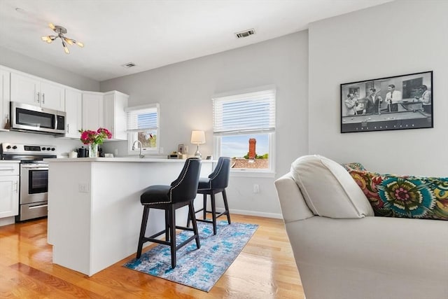 162 Willow Rd Unit 11, Nahant, MA 01908 - kitchen featuring stainless steel appliances, a kitchen bar, white cabinets, light wood-type flooring, and light countertops