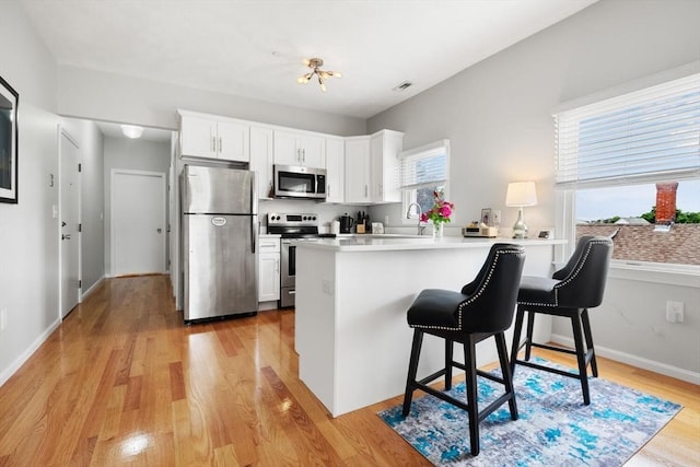 162 Willow Rd Unit 11, Nahant, MA 01908 - kitchen featuring stainless steel appliances, a kitchen bar, a peninsula, light wood-style flooring, and white cabinets