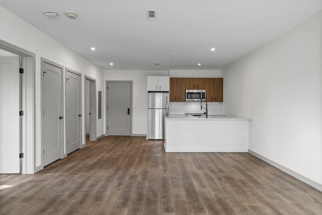 kitchen featuring wood-type flooring, backsplash, appliances with stainless steel finishes, white cabinets, and kitchen peninsula