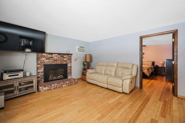 living area featuring a brick fireplace, baseboards, wood-type flooring, and a wall mounted AC