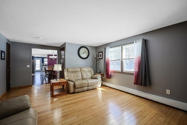 living room featuring light wood-type flooring, baseboards, baseboard heating, and an inviting chandelier