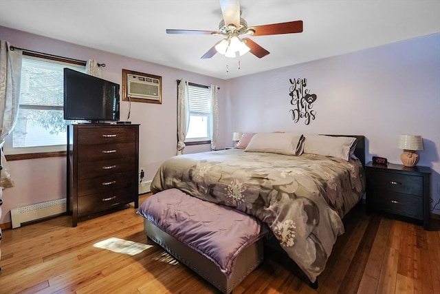 bedroom with baseboard heating, an AC wall unit, light wood-style flooring, and a ceiling fan