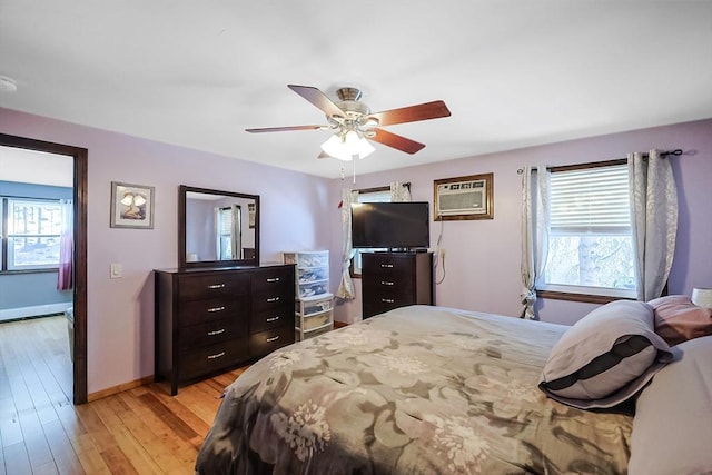 bedroom with an AC wall unit, baseboards, light wood-type flooring, and ceiling fan