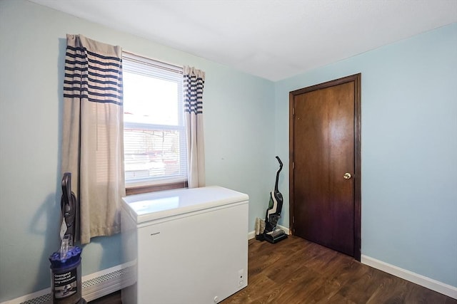 washroom featuring a baseboard radiator, dark wood-type flooring, baseboards, and laundry area