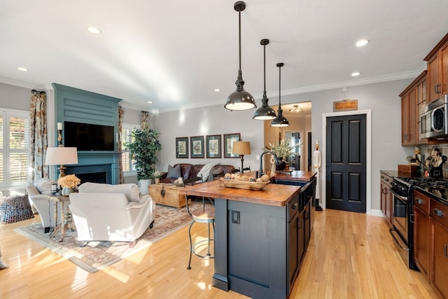 kitchen featuring appliances with stainless steel finishes, an island with sink, a fireplace, a kitchen breakfast bar, and light hardwood / wood-style floors