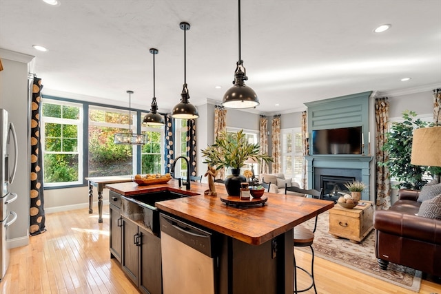 kitchen with light hardwood / wood-style floors, appliances with stainless steel finishes, a wealth of natural light, and an island with sink