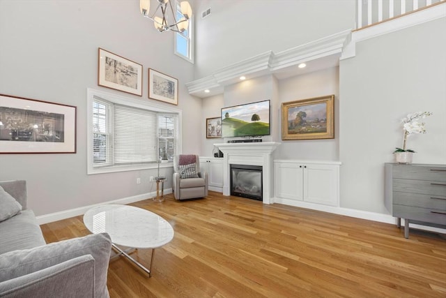 living area with a high ceiling, light hardwood / wood-style flooring, and a notable chandelier