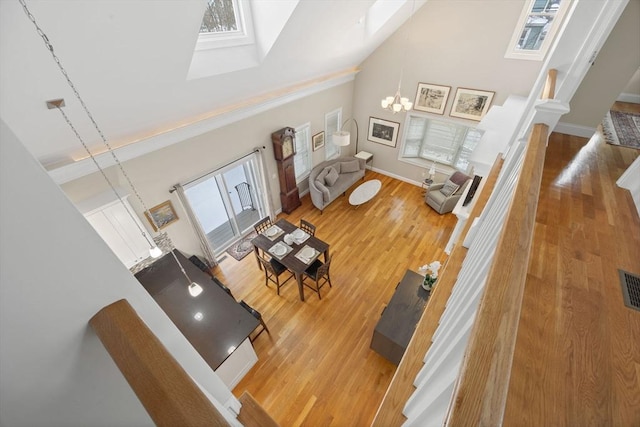 living room with a skylight, light wood-type flooring, an inviting chandelier, and high vaulted ceiling