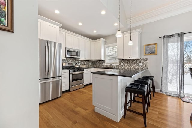 kitchen with stainless steel appliances, white cabinetry, a kitchen bar, kitchen peninsula, and hanging light fixtures