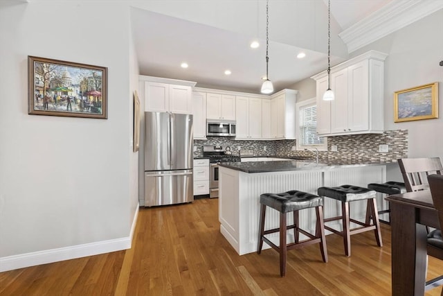 kitchen with appliances with stainless steel finishes, white cabinets, kitchen peninsula, hanging light fixtures, and dark wood-type flooring